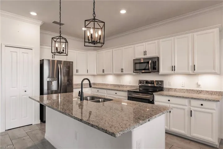 Kitchen featuring appliances with stainless steel finishes, crown molding, sink, a center island with sink, and white cabinets