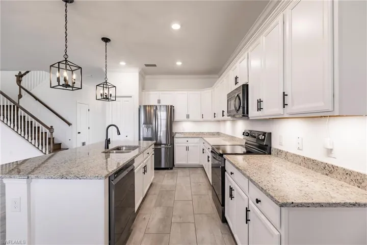 Kitchen featuring sink, black appliances, a center island with sink, white cabinetry, and hanging light fixtures