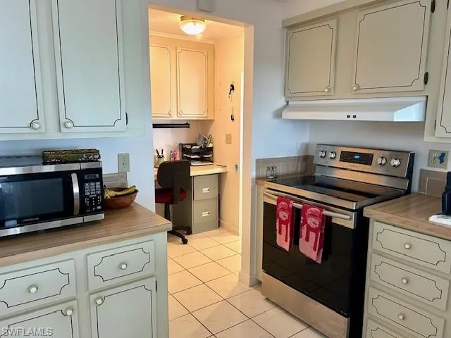 Kitchen featuring stainless steel appliances, light countertops, light tile patterned flooring, under cabinet range hood, and built in study area