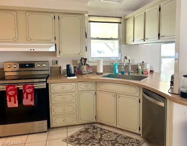 Kitchen with stainless steel appliances, light countertops, under cabinet range hood, light tile patterned floors, and cream cabinets