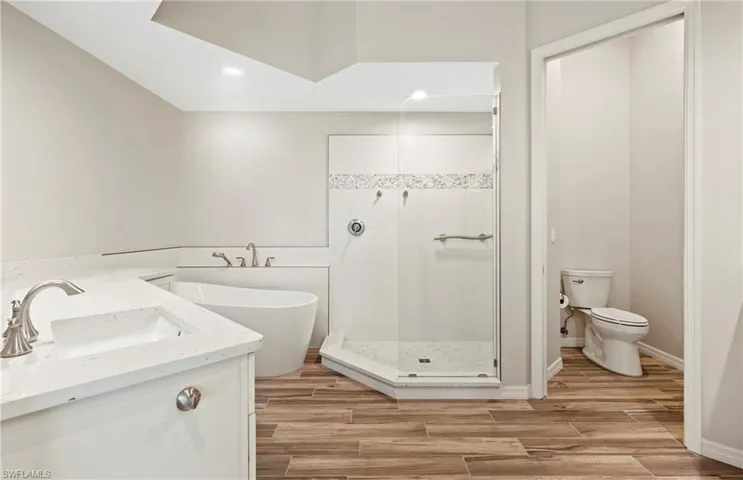 Bathroom featuring a soaking tub, toilet, a shower stall, a sink, and tile floors