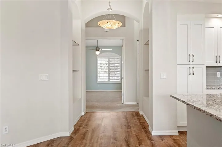 Hall with baseboards, arched walkways, and vinyl-style floors