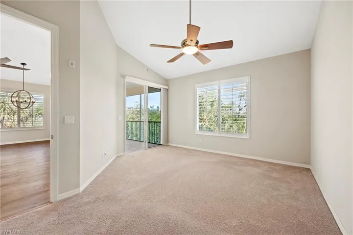 Unfurnished room with carpet, baseboards, vaulted ceiling, and ceiling fan with notable chandelier