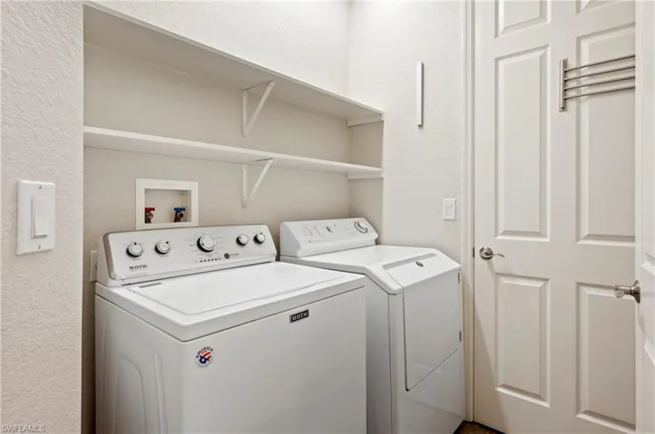 Laundry room with a textured wall, laundry area, and washing machine and clothes dryer