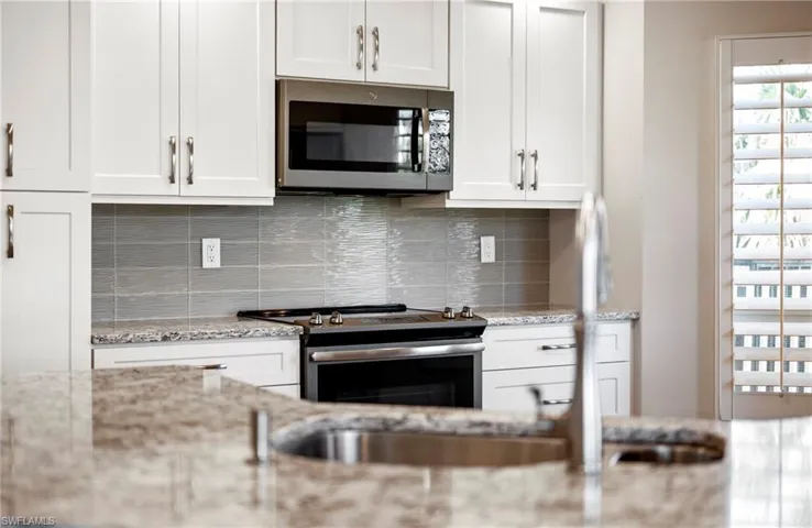Kitchen with tasteful backsplash, appliances with stainless steel finishes, light stone counters, and white cabinets