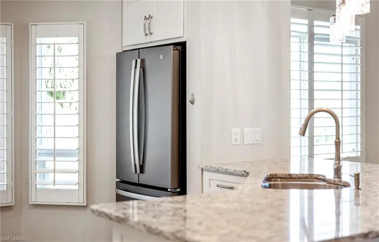 Kitchen featuring a sink, freestanding refrigerator, white cabinetry, and light stone countertops
