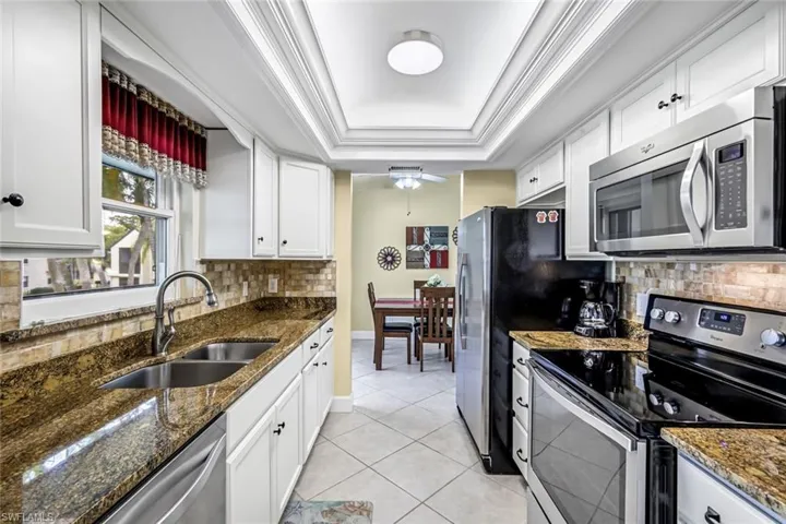 Kitchen with stainless steel appliances, white cabinetry, granite counters, and tray ceiling.