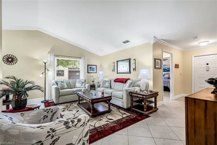 Living room featuring 18" tile flooring, vaulted ceiling, and crown molding.
