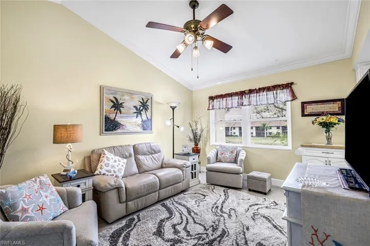 Den with crown molding, tiled floors, vaulted ceiling, ceiling fan, and healthy amount of natural light.