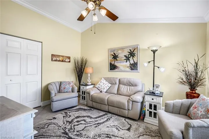 Den with crown molding, tiled floors, vaulted ceiling, ceiling fan, and healthy amount of natural light.