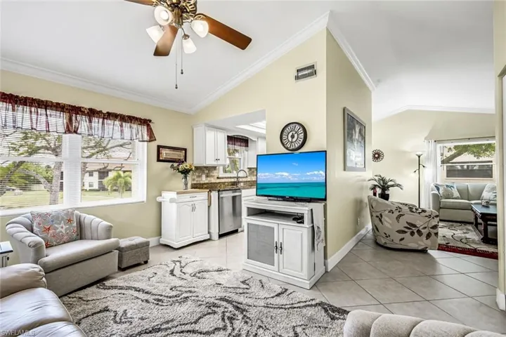 Living room with crown molding, tiled floors, vaulted ceiling, ceiling fan, and healthy amount of natural light.