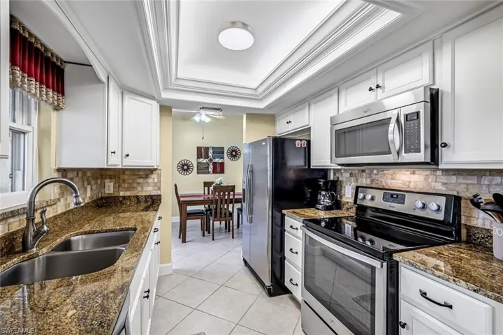 Kitchen with stainless steel appliances, white cabinetry, granite counters, and tray ceiling.