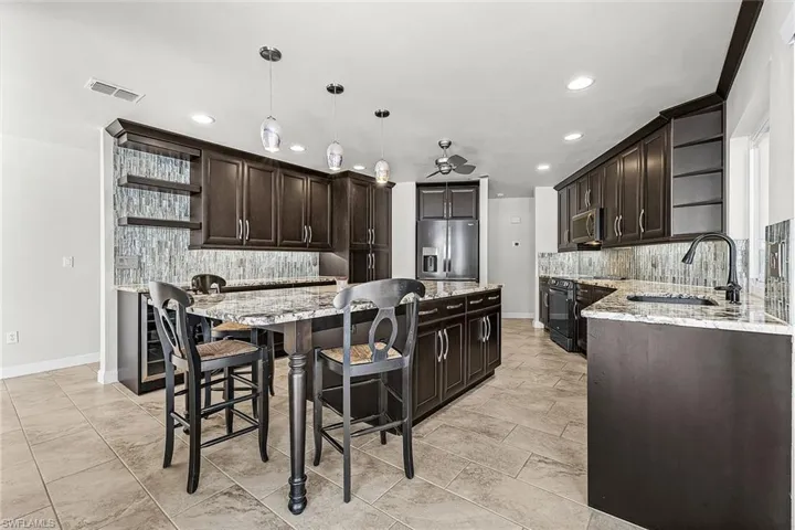 Kitchen featuring open shelves, decorative backsplash, dark brown cabinetry, light stone countertops, and recessed lighting and breakfast bar
