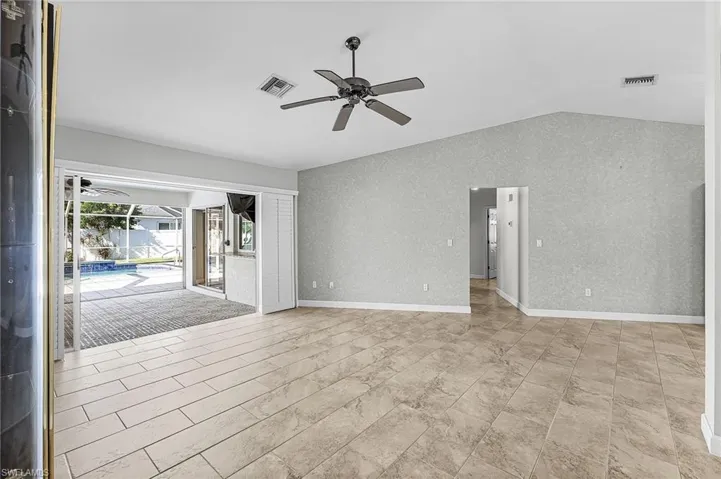 Unfurnished living room featuring a sunroom, a ceiling fan, vaulted ceiling, and wallpapered walls