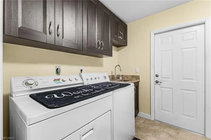Washroom featuring washing machine and clothes dryer, cabinet space, and light tile patterned flooring with access to the garage