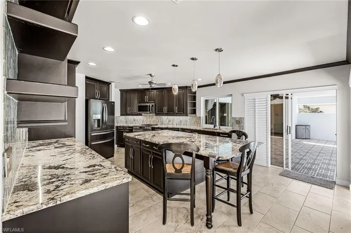 Kitchen featuring dark brown cabinets, decorative light fixtures, a kitchen island, recessed lighting, and light granite countertops, sliders to lanai, pass thru window
