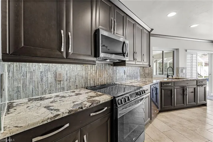 Kitchen with appliances with stainless steel finishes, light stone counters, dark brown cabinets, recessed lighting, and decorative backsplash