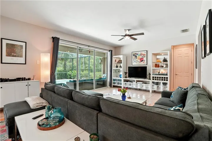 Bright and inviting open-concept living room with tile floors, recessed lighting, and a modern ceiling fan. Large sliding glass doors showcase serene pool and preserve views, filling the space with natural light. Seamless flow to the dining area and updated kitchen with dark cabinetry and stylish backsplash makes entertaining effortless. Perfect for Florida living, this spacious layout connects indoor comfort with outdoor enjoyment—ideal for families or seasonal retreats near Gulf beaches.
