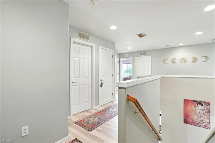 Bright and airy upstairs hallway with recessed lighting, neutral gray walls, and modern wood-look flooring. Multiple doors lead to spacious bedrooms and baths, while decorative wall accents and stylish rugs add warmth and character. The open railing overlooks the lower level, creating a connected, open feel. Perfect for families or guests, this versatile upper-level layout enhances functionality and flow in this beautiful Southwest Florida home
