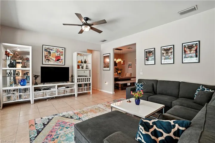 Bright and inviting open-concept living room with tile floors, recessed lighting, and a modern ceiling fan. Large sliding glass doors showcase serene pool and preserve views, filling the space with natural light. Seamless flow to the dining area and updated kitchen with dark cabinetry and stylish backsplash makes entertaining effortless. Perfect for Florida living, this spacious layout connects indoor comfort with outdoor enjoyment—ideal for families or seasonal retreats near Gulf beaches.