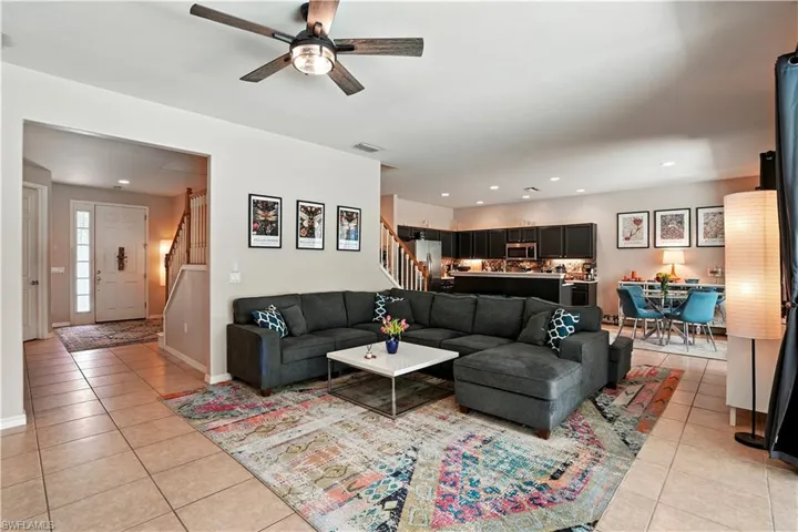 Bright and inviting open-concept living room with tile floors, recessed lighting, and a modern ceiling fan. Large sliding glass doors showcase serene pool and preserve views, filling the space with natural light. Seamless flow to the dining area and updated kitchen with dark cabinetry and stylish backsplash makes entertaining effortless. Perfect for Florida living, this spacious layout connects indoor comfort with outdoor enjoyment—ideal for families or seasonal retreats near Gulf beaches.