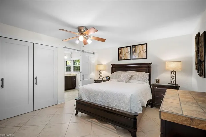 Bedroom featuring a barn door, light tile patterned flooring, ceiling fan, a closet, and ensuite bathroom