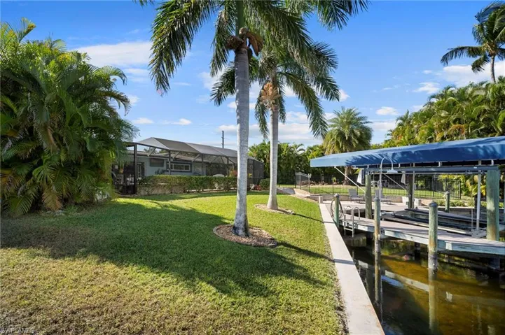 Dock featuring boat lift, a lanai, a water view, and a lawn