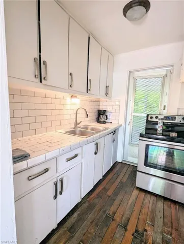 Kitchen featuring dark hardwood / wood-style floors, stainless steel electric range oven, tasteful backsplash, tile counters, and sink