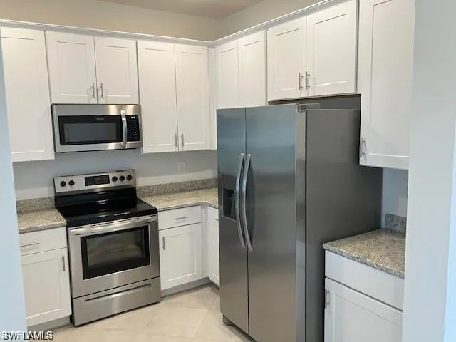 Kitchen featuring light tile patterned floors, stainless steel appliances, light stone counters, and white cabinetry