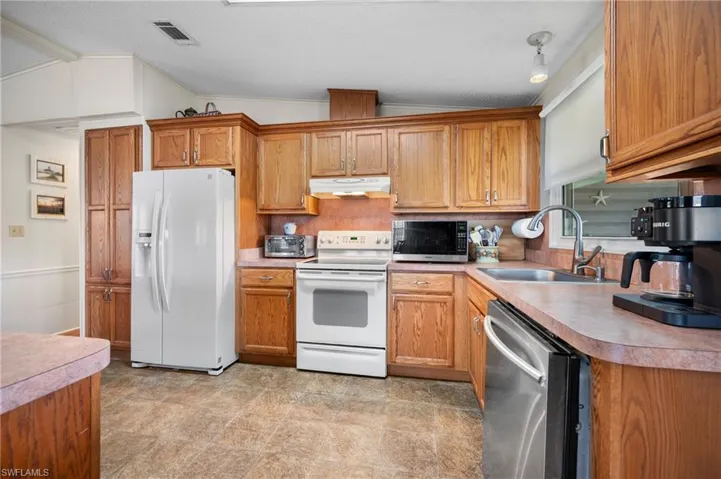 Kitchen with stainless steel appliances, vaulted ceiling, ornamental molding, brown cabinetry, and under cabinet range hood
