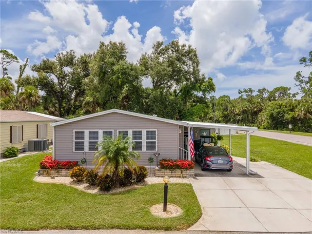 Manufactured / mobile home with a front yard, a carport, concrete driveway, and view of scattered trees
