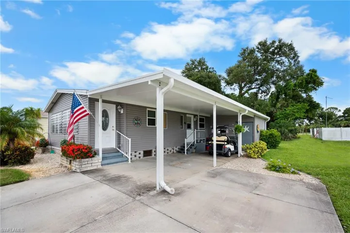 View of front of house with concrete driveway, a carport, and a front lawn