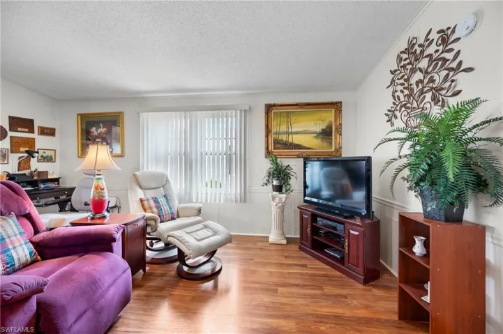 Living room featuring a textured ceiling, wood finished floors, ornamental molding, and wainscoting