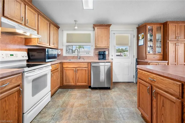 Kitchen with appliances with stainless steel finishes, under cabinet range hood, a textured ceiling, brown cabinets, and light countertops