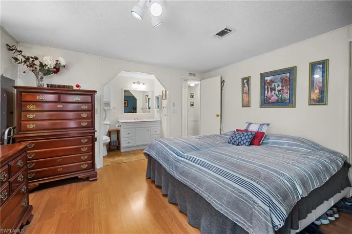Bedroom featuring light wood-style floors, a textured ceiling, and ensuite bath