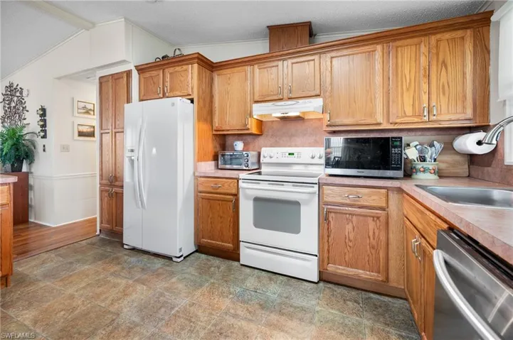 Kitchen with stainless steel appliances, brown cabinets, under cabinet range hood, light countertops, and crown molding