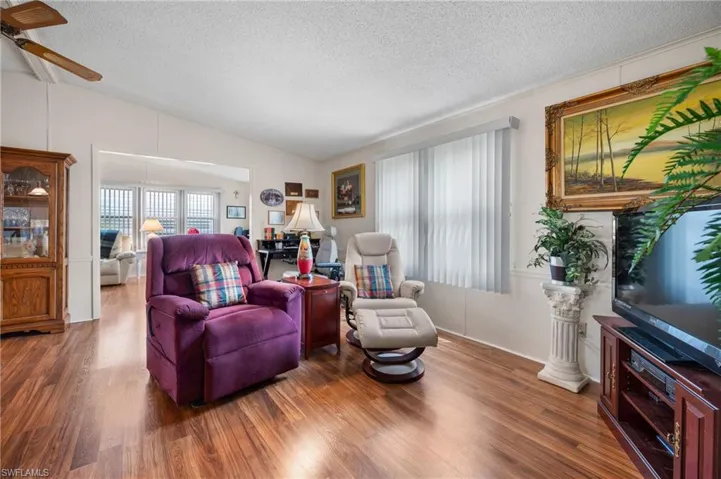 Living room featuring wood finished floors, a textured ceiling, lofted ceiling, and ceiling fan