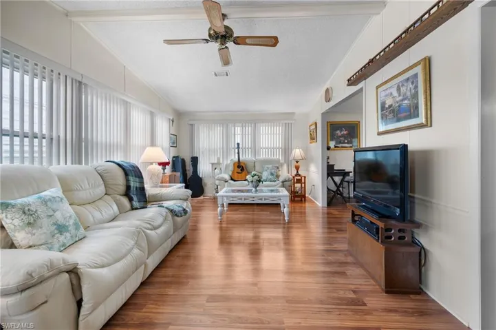 Living area with a textured ceiling, wood finished floors, a ceiling fan, a decorative wall, and lofted ceiling