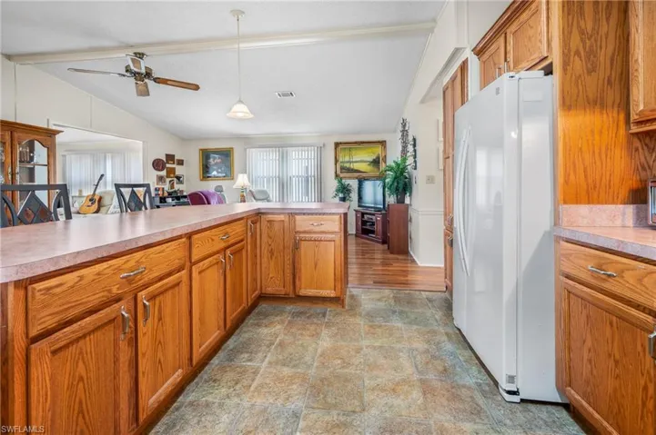 Kitchen with freestanding refrigerator, brown cabinets, light countertops, ceiling fan, and pendant lighting