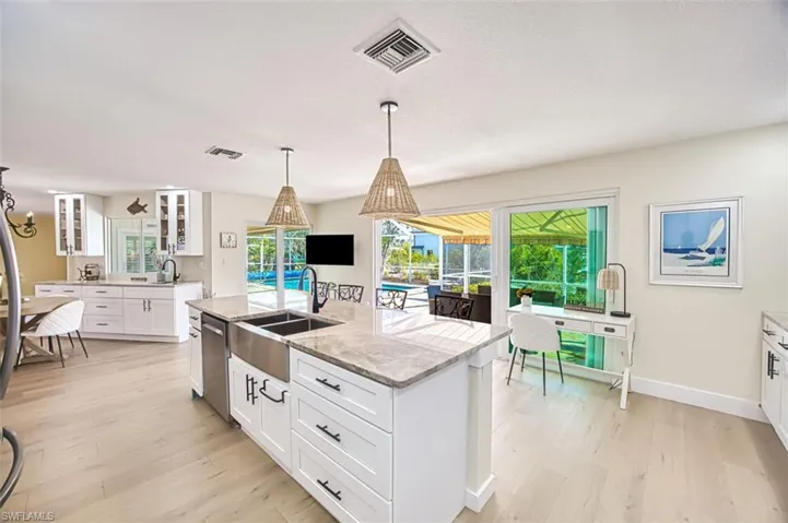 Kitchen with white cabinetry, light stone counters, glass insert cabinets, a center island with sink, and light wood-style floors