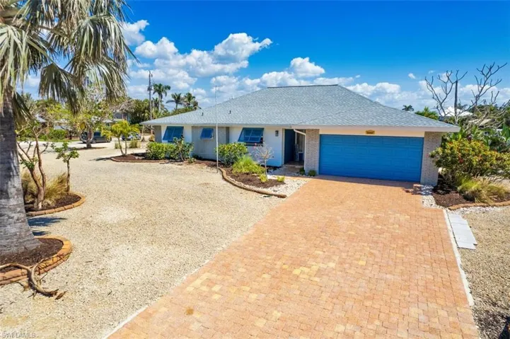 Ranch-style home featuring decorative driveway, roof with shingles, brick siding, and a garage
