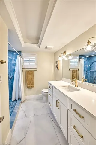 Full bathroom with curtained shower, vanity, light marble finish flooring, and healthy amount of natural light