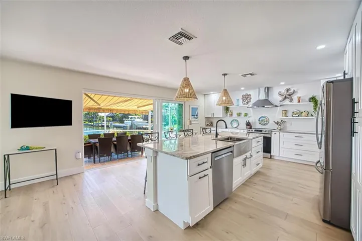 Kitchen with white cabinets, open shelves, stainless steel appliances, light stone counters, and a kitchen bar