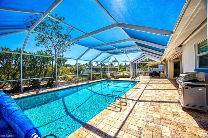Outdoor pool featuring area for grilling, a sunroom, a patio area, and glass enclosure