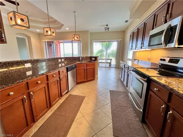 Kitchen featuring stainless steel appliances, pendant lighting, dark stone countertops, a raised ceiling, and light tile patterned floors
