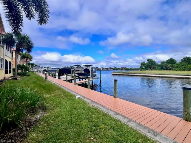 Dock with a lawn, a water view, and boat slip with lift and electric and water at the dock
