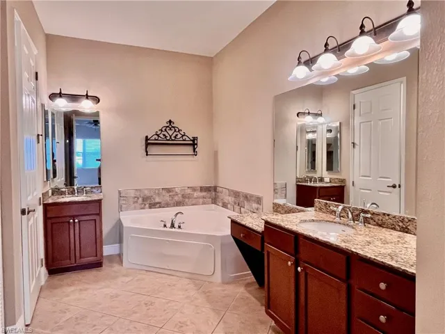 Primary Bathroom with two vanities, a jetted bath tub, and light tile floors, his and her walk in closets