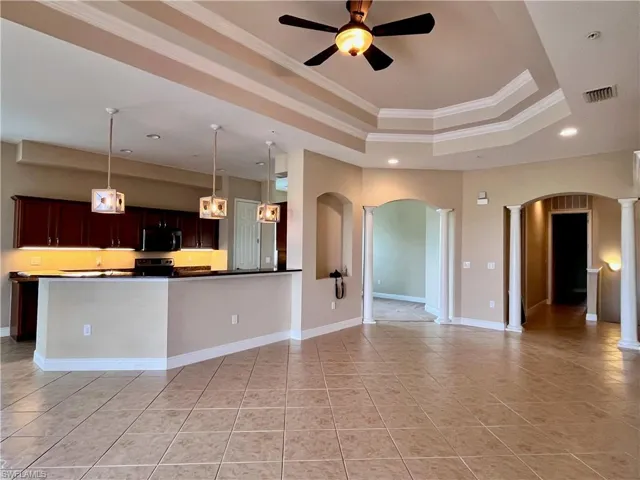 Kitchen featuring crown molding, hanging light fixtures, a tray ceiling, dark countertops, and open floor plan