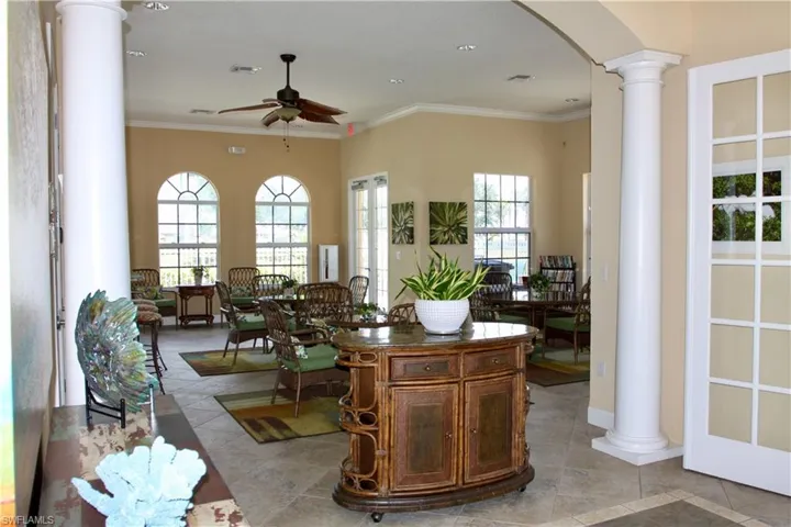 Main sitting area of the clubhouse features ornate columns, ornamental molding, light tile patterned floors, arched walkways, and a ceiling fan