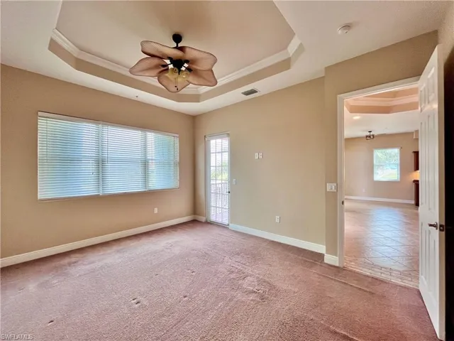 Primary bedroom with ensuite bathroom, his and her walk in closets with a tray ceiling, light colored carpet, crown molding, and a ceiling fan